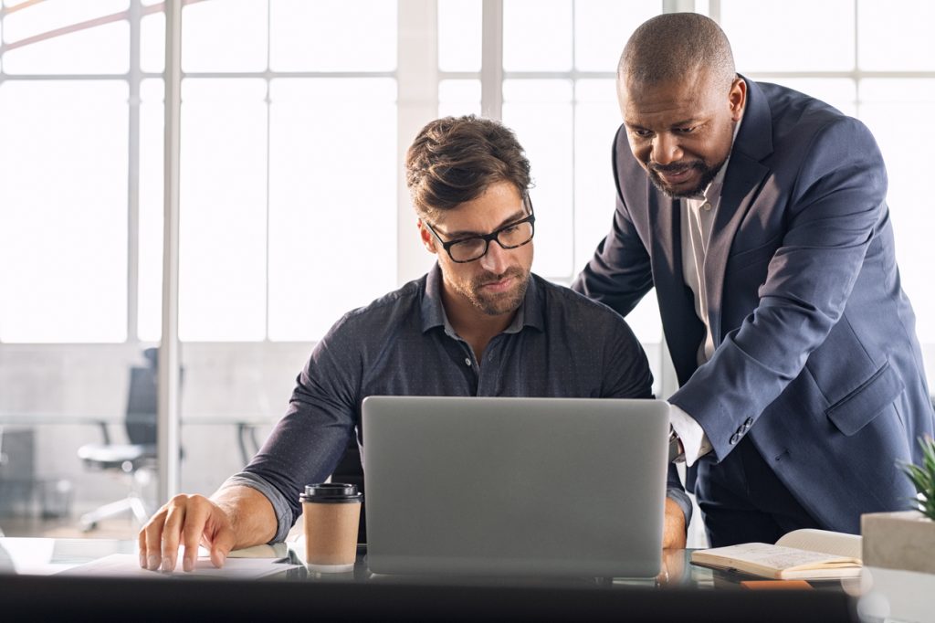 Business multiethnic colleagues having meeting in modern office. Smart business partners planning work together. Young businessman with boss working together on laptop.