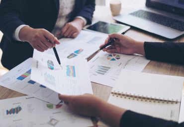 close up hand of marketing manager employee pointing at business document during discussion at meeting room , Notebook on wood table - Business concept