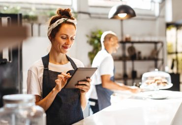 Cafe waitress using a digital tablet to manage orders. Woman using a touchscreen device that helps her to view and organize orders effectively, ensuring prompt and efficient service for the customers.